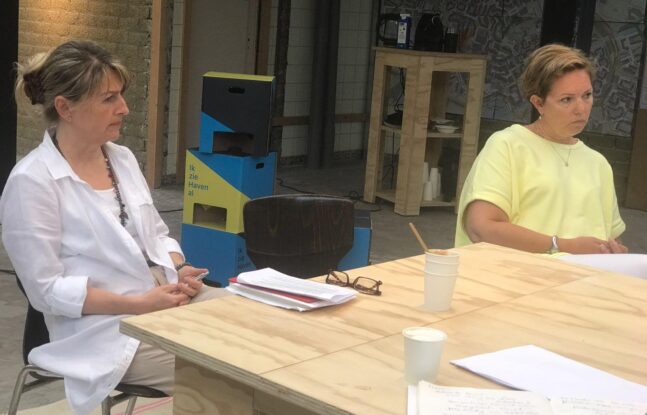 Twee mensen zitten aan een tafel en luisteren aandachtig naar iemand buiten beeld