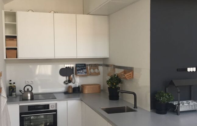 Een keuken met witte kastjes en een grijs aanrechtblad onder een schuin dak