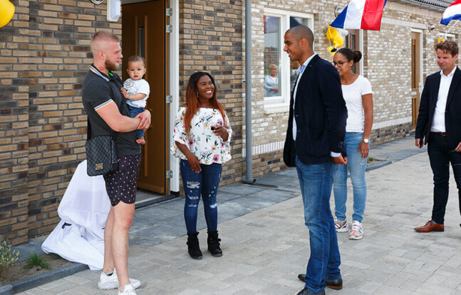 Een paar mensen staan voor een rijtjes woning waaraan Nederlandse vlaggen hangen