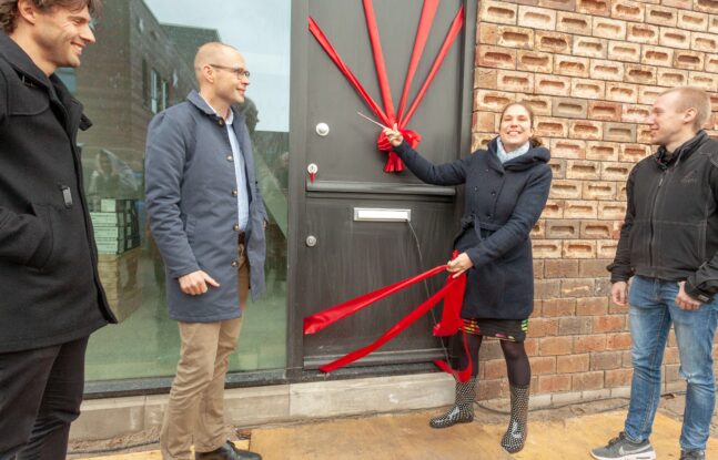 De wethouder knipt een lint door bij de voordeur van een nieuwe woning