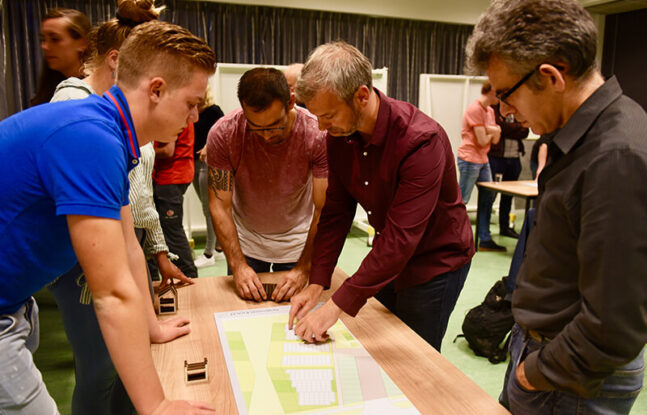 Mensen staan om een tafel met daarop een bouwtekening