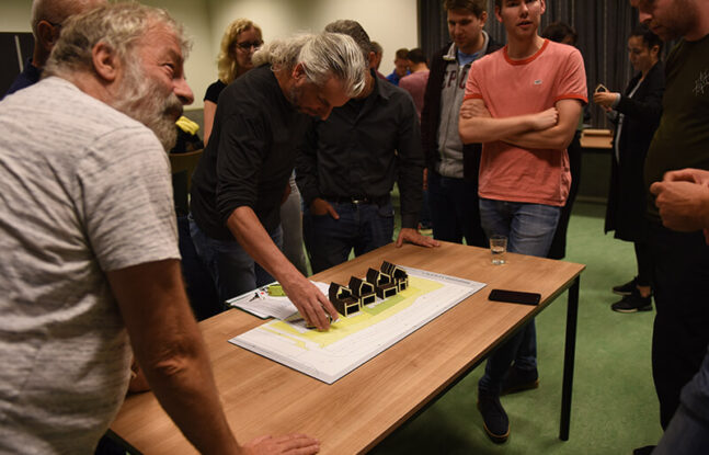 Mensen staan om een tafel met daarop miniatuurversies van Tinyhouses op een plattegrond