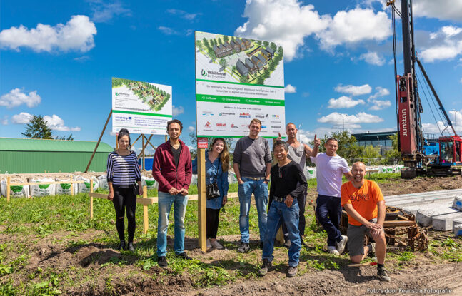 Groep van acht personen poseert op een zonnige dag voor een bouwbord van WikiHouse