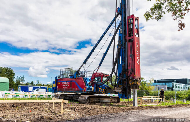 Een grote heimachine is bezig met het heien van palen in de grond