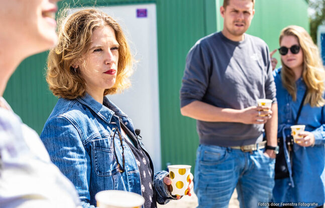 Vier mensen staan met een bekertje in hun hand op een zonnige dag te wachten