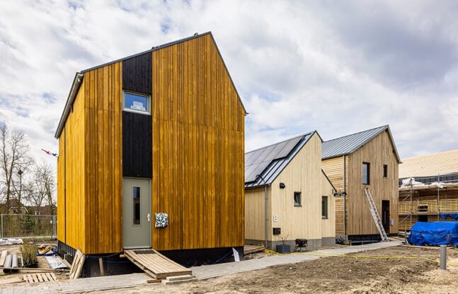 Een rij opgeleverde Wikihouses naast een Wikihouse in aanbouw