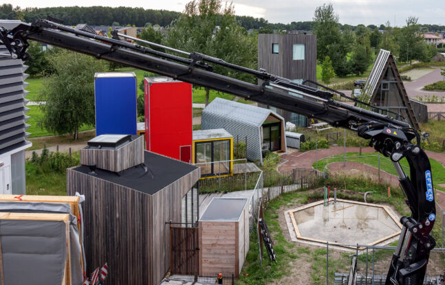 Een zwarte kraan op een bouwplaats bij een groep met tiny houses.