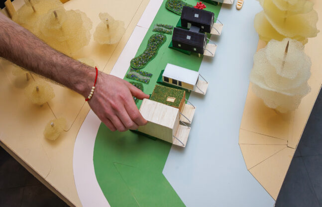 Iemand plaatst een huisje op de maquette