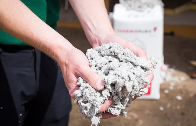 Een persoon houdt een handvol met cellulose isolatiemateriaal vast