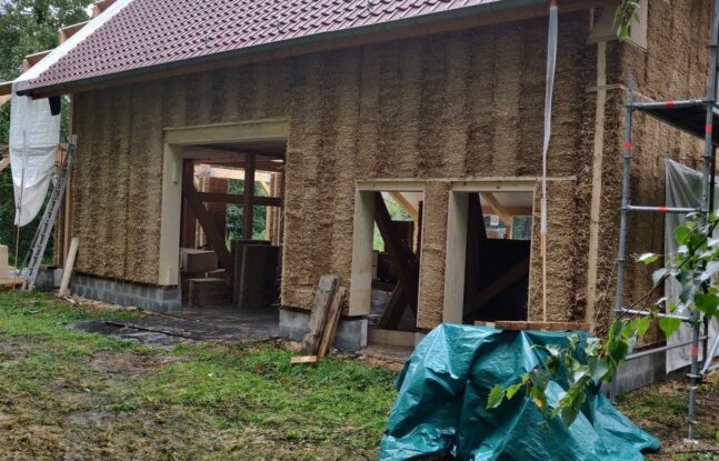 Een huis met wanden gemaakt van stro en op het dak rode dakpannen
